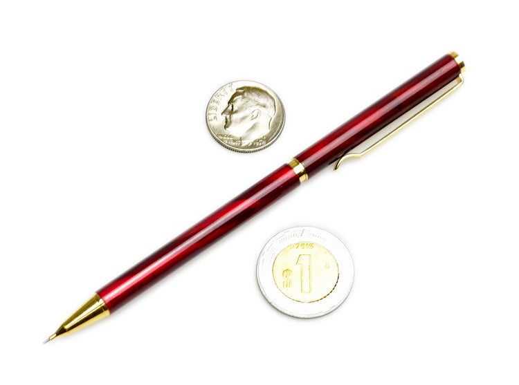 A red and gold pen is placed on a white surface next to a U.S. dime and a Japanese 1 yen coin.