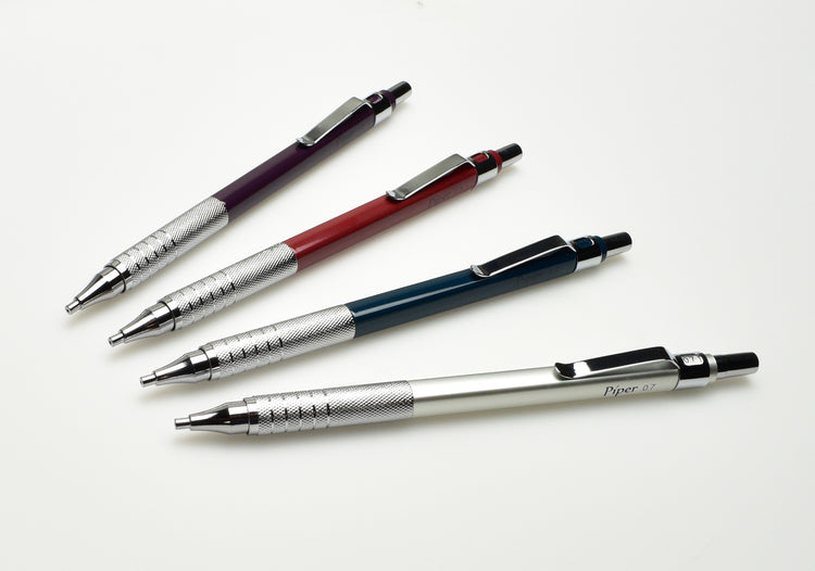 Four mechanical pencils in purple, red, blue, and silver with metal grips and clips are arranged diagonally on a white background.
