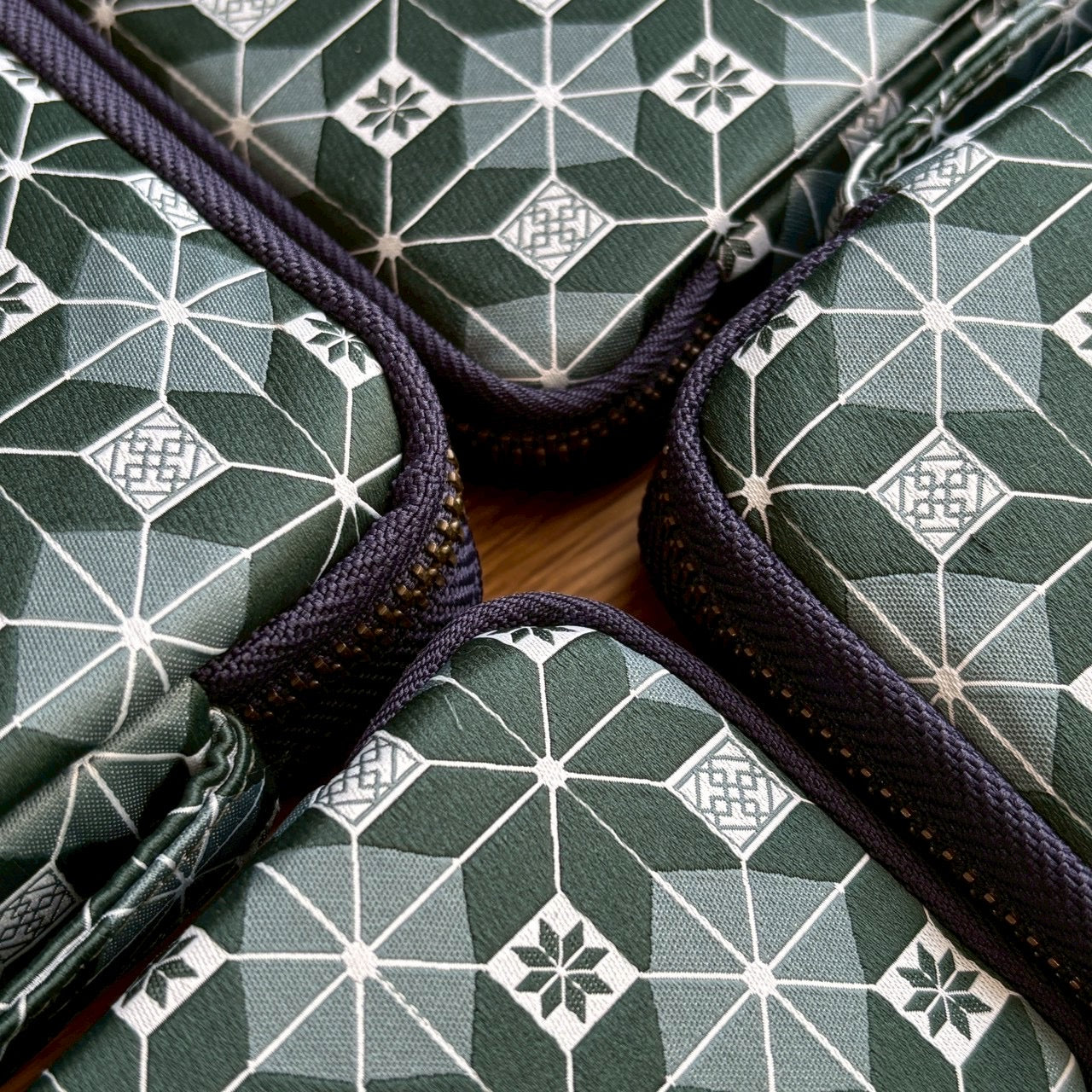 Four Kyoku Haku Restitch Emerald 10 Pen Cases with Pocket by Piper Trading Co. are shown in a close-up arrangement, their corners meeting at the center to create a striking symmetrical display. Each green zippered pouch features geometric white and dark green patterns inspired by Siraya embroidery, making them a stylish option for pen storage or stationery organization.