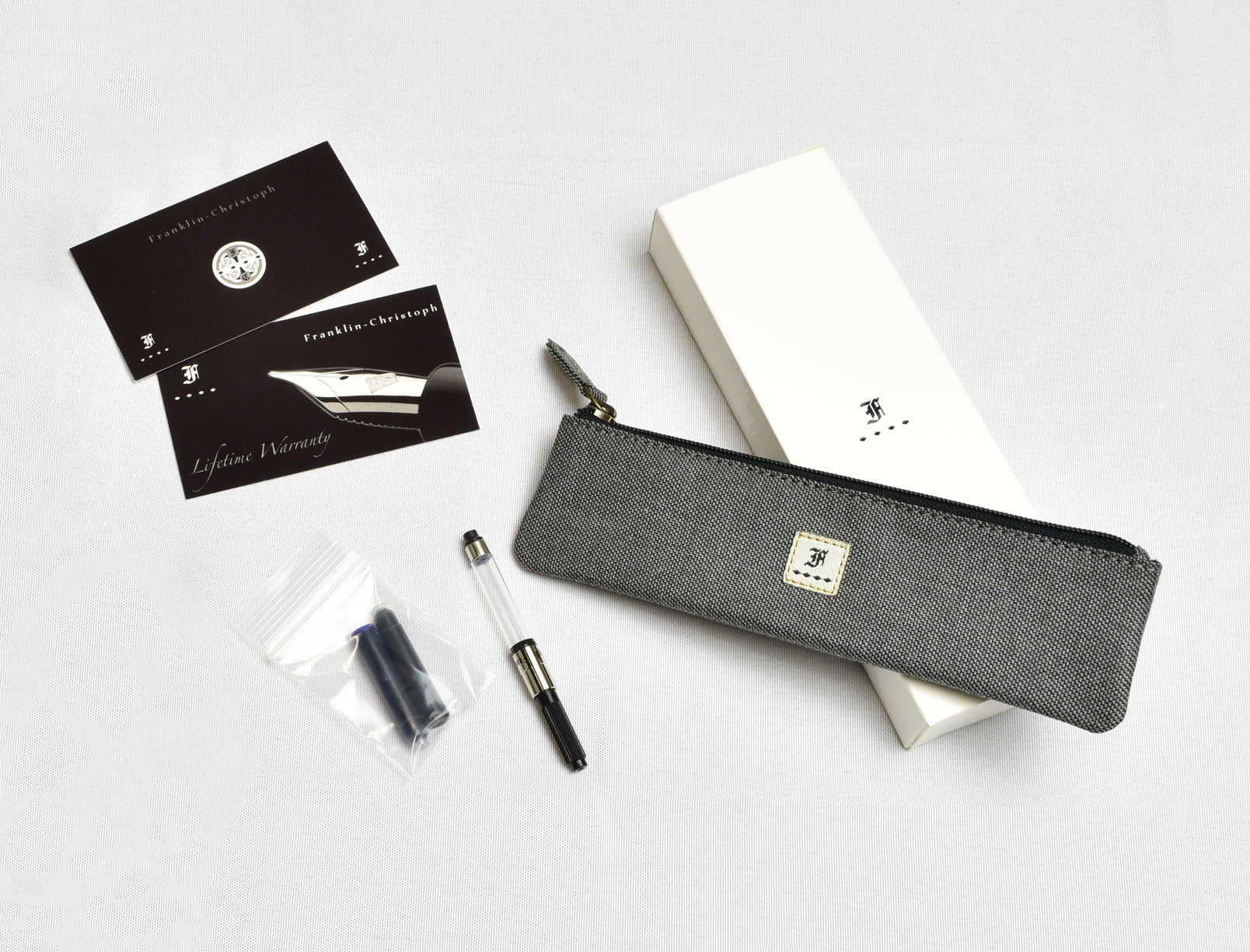 A Piper Trading Co. Franklin-Christoph Model 46 Fountain Pen in Venetian Red, featuring a Franklin-Christoph nib, an ink cartridge, warranty cards, a gray zippered pen pouch, and a white box are arranged on a white surface.